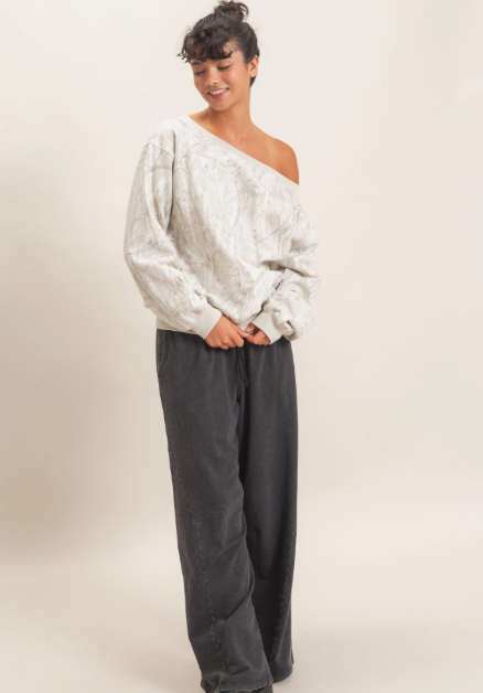 A model wearing a light gray textured off-the-shoulder long-sleeve top and dark gray wide-leg pants, standing against a plain beige studio background.
