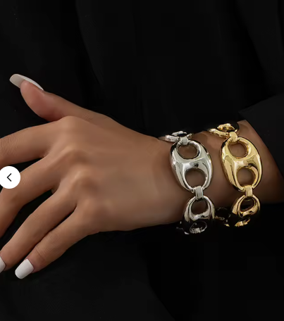 A close-up of a person's hand wearing two chunky interlocking chain bracelets, one silver-toned and one gold-toned, against a black outfit background.