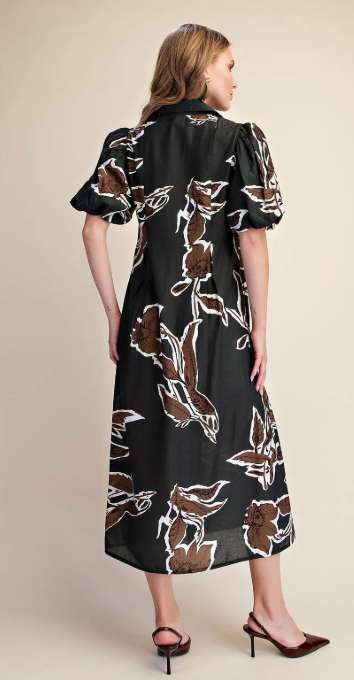 A woman modeling a black midi dress with brown and white floral patterns, shown from the back against a solid beige background.