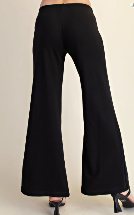 Black wide-leg flare pants shown from the back on a model, paired with black high heels against a plain beige studio background.