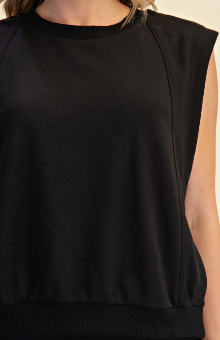 Close-up of a person wearing a black sleeveless top with a crew neck and ribbed trim, against a plain light background.