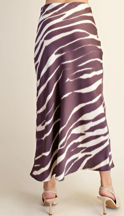 A woman's midi skirt with a zebra print pattern in dark purple and white, shown from the back on a model wearing beige high-heeled sandals against a plain beige background.