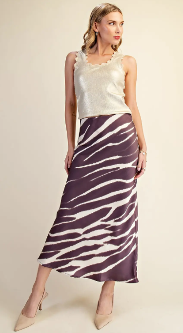 A woman models a sleeveless metallic champagne top and a high-waisted midi skirt with a purple and cream zebra stripe pattern, set against a plain beige studio background.