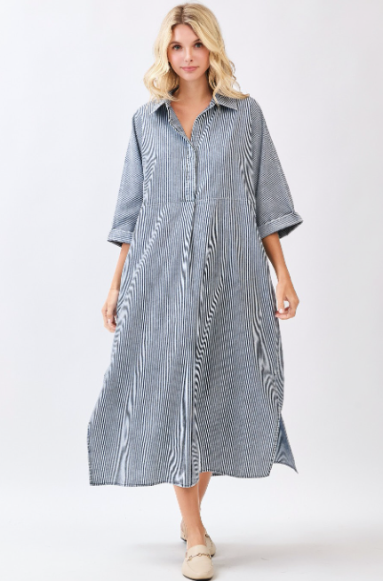 A woman modeling a long-sleeve midi shirt dress with vertical blue and white stripes, photographed against a plain light gray studio background.