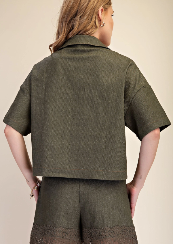 A woman shown from the back wearing a matching olive green short-sleeve collared top and high-waisted shorts with lace trim at the hem, against a plain beige studio background.