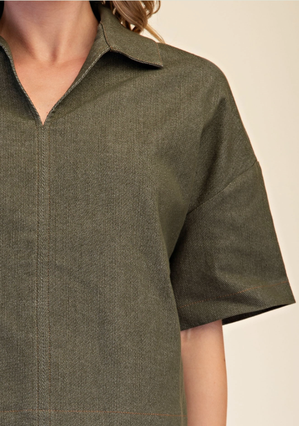 Close-up of a model wearing an olive green short-sleeve collared shirt with a textured weave, set against a plain beige background.