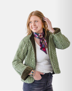 A woman modeling a green and white vertically striped jacket with dark brown trim, styled with a colorful patterned neck scarf, a white top, and blue jeans against a plain white background.