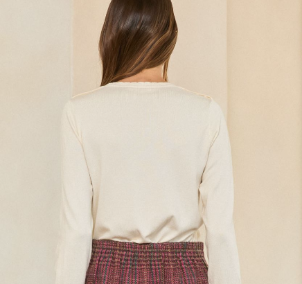 A woman shown from behind wearing a cream ribbed long-sleeve top and a red and green tweed skirt, set against a minimalist beige background.