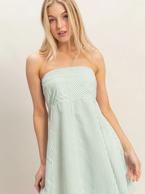 Woman wearing a strapless green dress with white stripes on a plain background