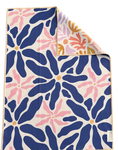 A folded textile product, likely a blanket or towel, featuring a bold abstract floral pattern in navy blue, pink, and orange on a cream background. The top-right corner is folded over to show the reverse side with a different pattern.