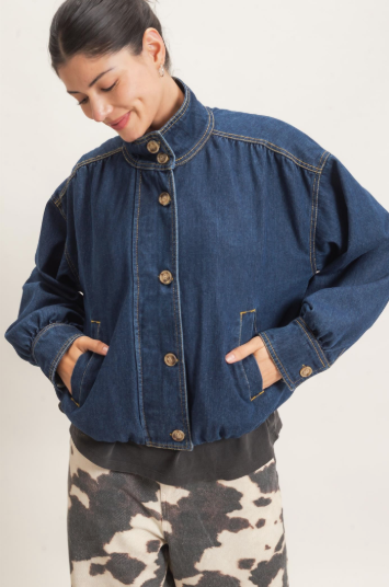 A woman wearing a cropped dark blue denim jacket with a high collar and front buttons, paired with black and white cow-print pants, against a plain light background.