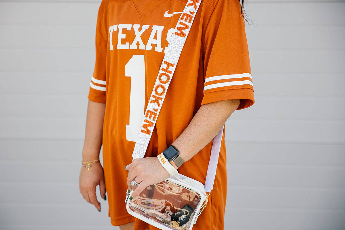 Person wearing an orange 'Texas Longhorns' jersey holding a clear handbag with a gray background