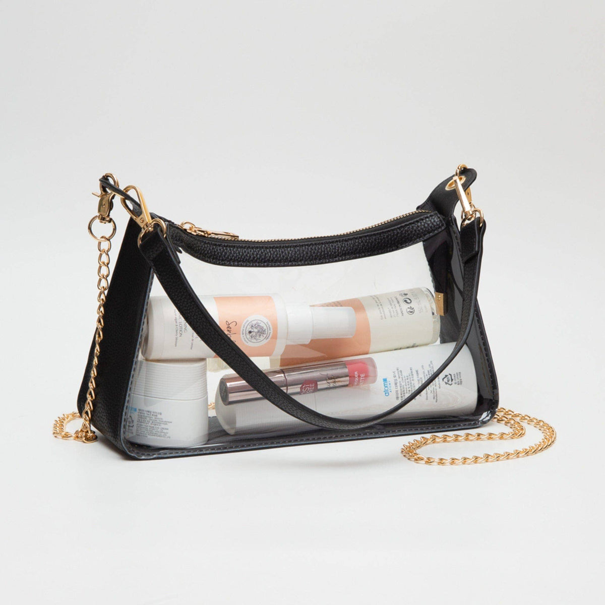 Black handbag with gold chain strap containing skincare products on a white background