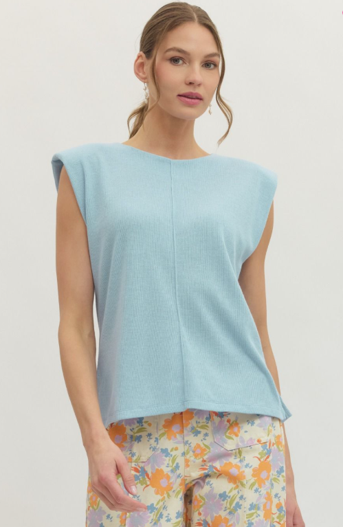 Woman wearing a light blue sleeveless top with floral pants on a plain background