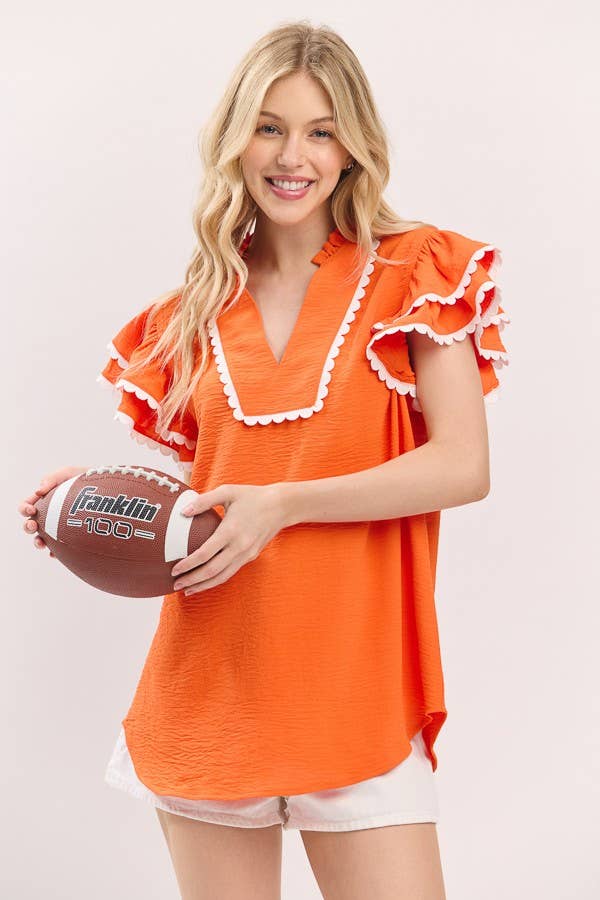 Woman wearing an orange top with white trim holding a football on a plain background