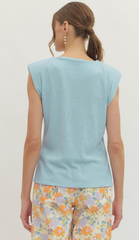 Woman wearing a light blue sleeveless top and colorful floral pants on a plain background